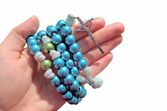 Hand holding a blue and green rosary with a silver crucifix on a white background