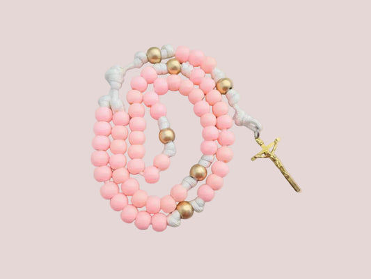 Light pink and gold beaded paracord rosary with a gold colored crucifix on a light pink background.