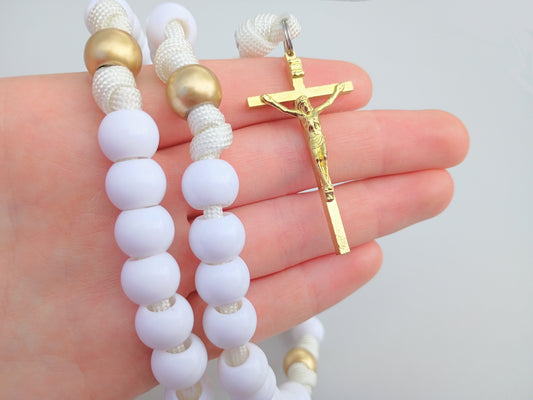 White and gold beaded rosary held in a hand against a white background