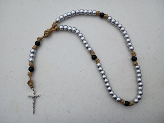 Durable paracord rosary with shiny silver beads and matte black beige/gold accents on a light gray background