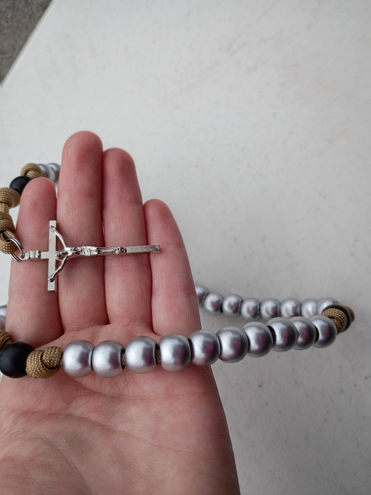 Hand holding a rosary with a silver cross and shiny silver beads on a light background